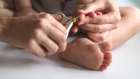 Close-up mom cuts off the baby's nails on the leg on white background Stock Footage 249737335
