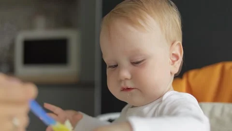 Close-up. Mom feeds a small child with a spoon. A little boy sits in a feeding Stock Footage 133439844