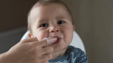 Close-up of mom hands clean the first teeth of her little baby son in the mornin Stock Footage 126486751