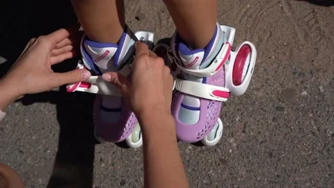 Close-up Mom putting on inline skates rollers to daughter child in public park Stock Footage 237892743