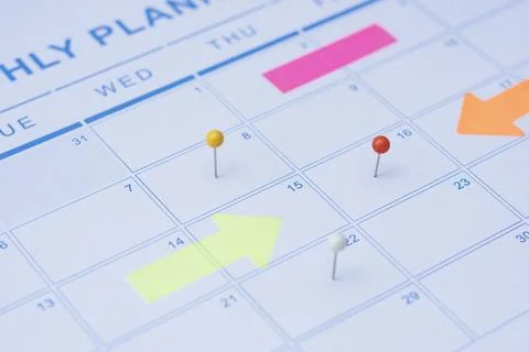 Close up of a monthly wall calendar featuring push pins and bright arrow post Stock Photos
