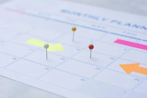 Close up of a monthly wall calendar featuring push pins and bright arrow post Stock Photos
