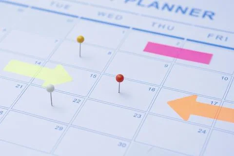 Close up of a monthly wall calendar featuring push pins and bright arrow post Stock Photos
