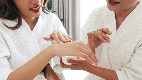 Close-up of a mother applying lotion to her daughters hand, both in white robes. Stock Footage 309754485
