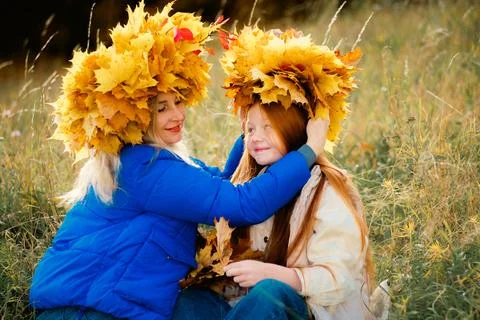 A close-up of a mother in a blue jacket adjusting a large yellow maple leaf.. Photos