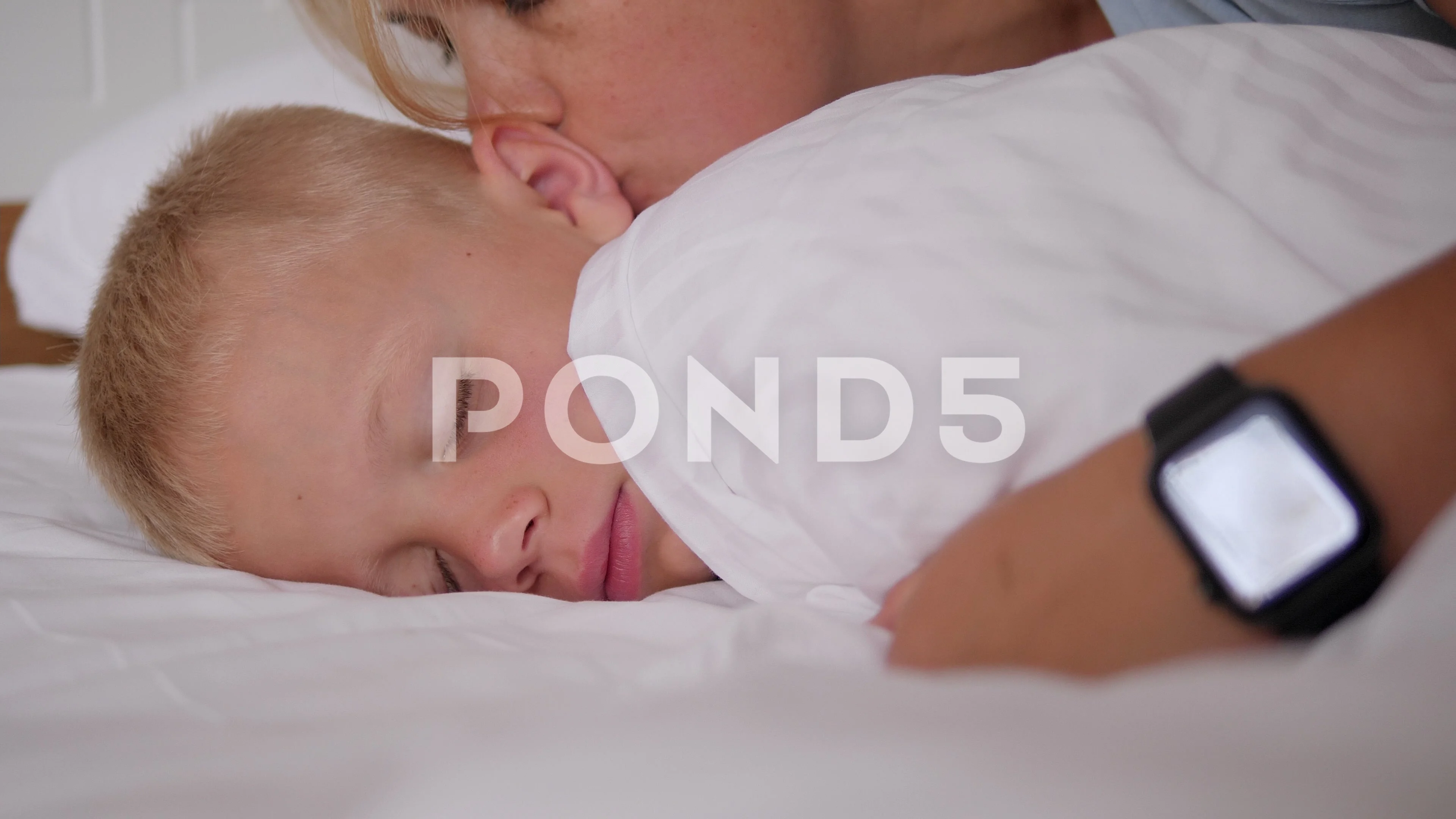 Close-up of a mother kissing her sleeping son in bed in the morning.