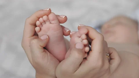 Close up of mother's hands holding tiny legs of newborn son Stock Footage 172167532