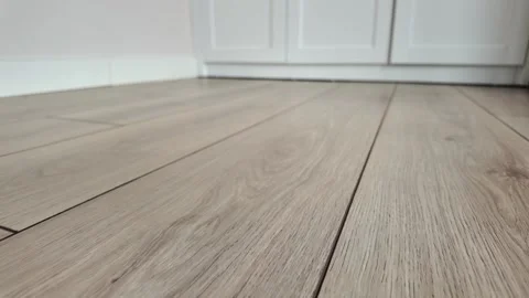 Close up motion of light brown laminate flooring with white baseboard. Stock Footage 332471177