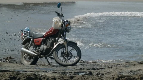 Close up of motorcycle on beach with waves during day time Stock Footage 143016523
