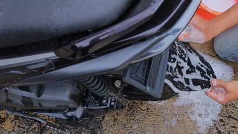 Close-up of motorcycle owner brushing dirty mudguard with soap outdoors Vidéo 336701237
