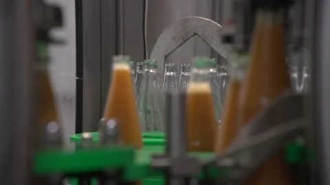 Close up of moving orange-colored juice and empty bottles inside bottling line Stock Footage 163892402