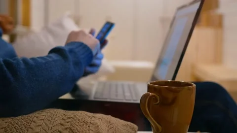 Close-up of a mug of coffee, an unrecognizable man sits on the couch, uses a Stock Footage 171555400