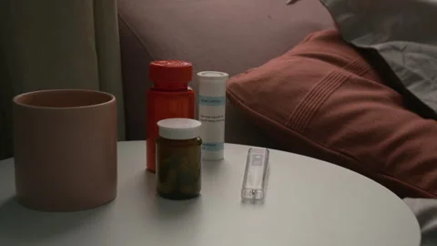 Close-Up of Mug, Three Pill Bottles and Thermometer on White Bedside Table Stock Footage 335468134