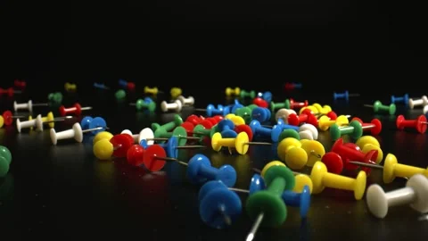 Close-up of Multi Colored push pins jumping and lying on black surface. Office Stock Footage 144342679