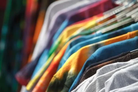Close-up of multi-colored T-shirts hanging on hangers in the street, fair, se Stock-Fotos