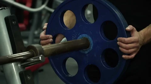 Close-up of multi-ethnic man puts metal disc on sports projectile for strength Video stock 93962937