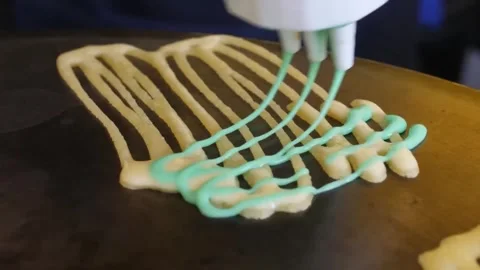 Close-Up of Multi-Nozzle Dispenser Pouring Colorful Batter for Lace Crepes on Gr Stock Footage 345692598