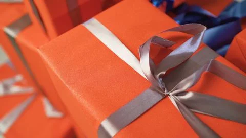 Close up of multiple bright orange gift boxes wrapped with shiny silver and blue Foto stock