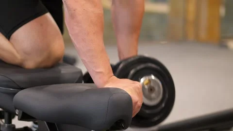 Close-up of a muscular man doing one-arm dumbbell rows on a bench in a mode.. 스톡 동영상 344049177