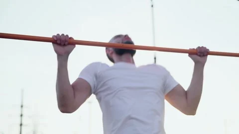 Close up of muscular man doing pull-ups on horizontal bar. On workout area near Video stock 143502542
