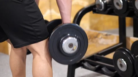 Close-up of a muscular man picking up heavy dumbbells from the floor near a.. Video stock 344052958