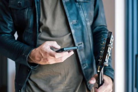 Close up of musician in leather jacket using smartphone guitar app while ho.. Stock Photos