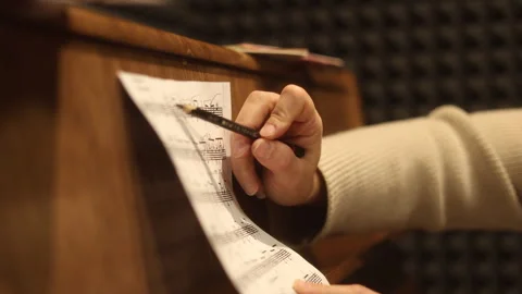 Close-up of a musician's hand writing on sheet music with a pencil Stock Footage 337666644