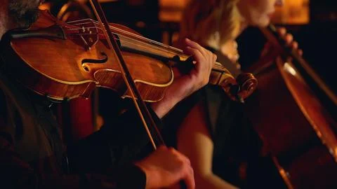 A close-up of musicians playing string instruments in an orchestra, focusing  Stock Photos