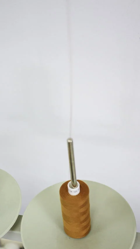 Close up of a mustard yellow thread cone on a thread stand, with a fine strand Stock Footage 335504055