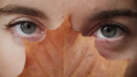 Close up of mysterious Woman's face covered by autumn leaf opening blue eyes. Stock Footage 142908607