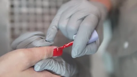 Close-up of a nail technician applying bright red nail polish on a clients Stock Footage 311872642