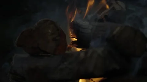 Close-up narrow focus campfire, stacked logs, orange blaze at dusk Stock Footage 312323547