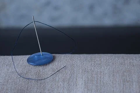 A close-up needle with a blue thread is inserted Stock Photos