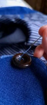 Close up of needle with blue thread sewing brown button on denim fabric concept Stockfoto's