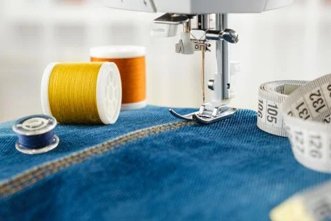 Close up of needle of sewing machine on denim fabric stitch, spools of threads. Stock Photos