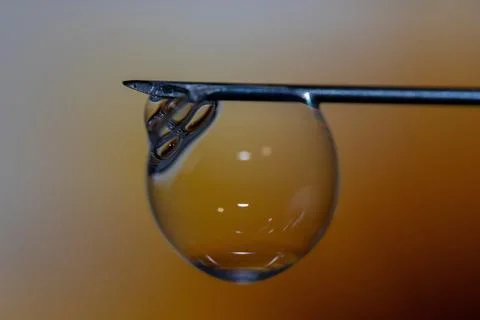 A close-up of a needle tip with a large drop of liquid and small bubbles form Stock Photos