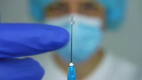 Close up of needle with vaccine ready to inject. Male doctor in background Видео 282662874