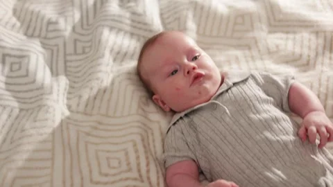 Close-up of a newborn baby lying on a patterned blanket, looking thoughtfully Vidéo 340629838
