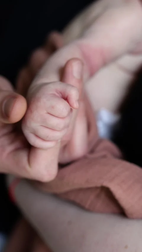 A close-up of a newborn baby’s tiny hand cradled in the loving hands of parents Stock Footage 303603606