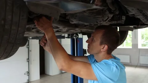 Close-up of a nice looking man in a blue uniform who repairs a car at a service Stock Footage 159220934