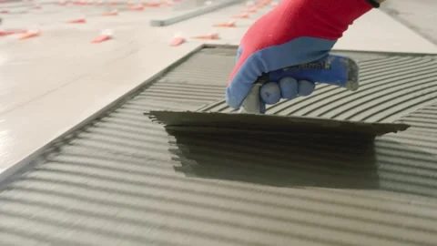 Close up of a notched trowel spreading tile adhesive on the floor of a Stock Footage 344059893
