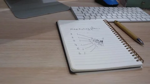 Close-up notebook with handwritten marketing plan strategy on modern office Stock Footage 332120678
