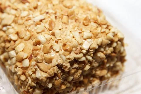 Close-up of nut-covered dessert bar in plastic container on light background Stock Photos