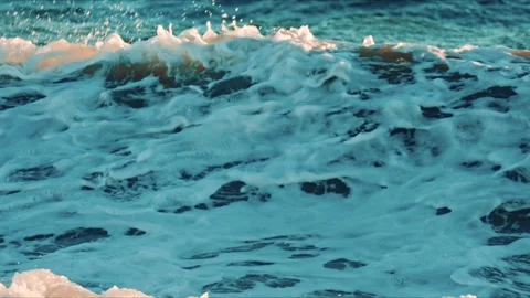 Close up of ocean foam washing over the sandy shore with deep blue waves behind Stock Footage 322958652