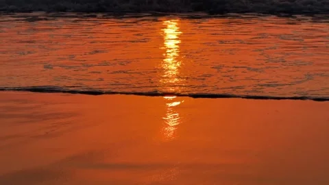 Close up ocean wave washing over wet sand with silhouettes of legs of passing 스톡 동영상 342219129