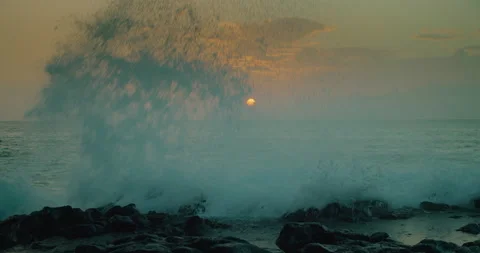 Close-up of ocean waves splashing on rocky beach at sunset with big sun on the Stock Footage 232899471