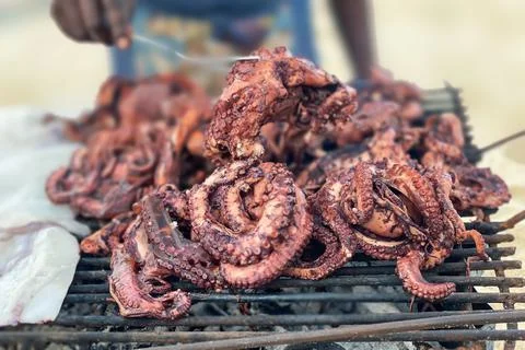Close-up of octopuses in the hands of a man fried on a grill on the ocean shore Stock Photos