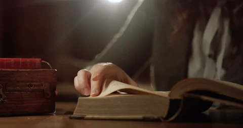 Close up of old antique book lying on table in dark room and female hand Stock Footage 125338629