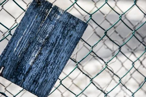 Close-up of an old cracked rectangular wooden slab on a green mesh fence 스톡 사진