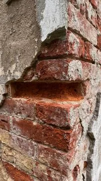 Close up of an old damaged red brick wall corner with peeling grey plaster and Stock Photos